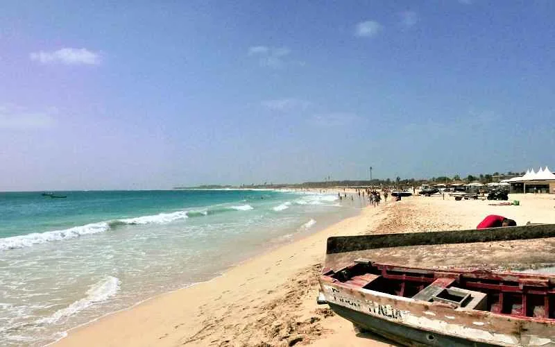 Une plage au cap vert, avec des paillotes au loin et des barques en gros plan sur le sable.