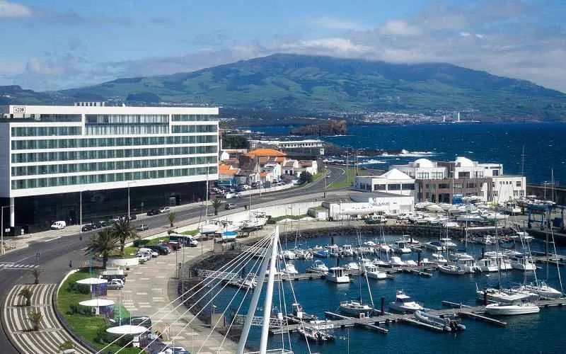 Une ville des acores sous le soleil, son port, la mer autour, et une montagne au loin